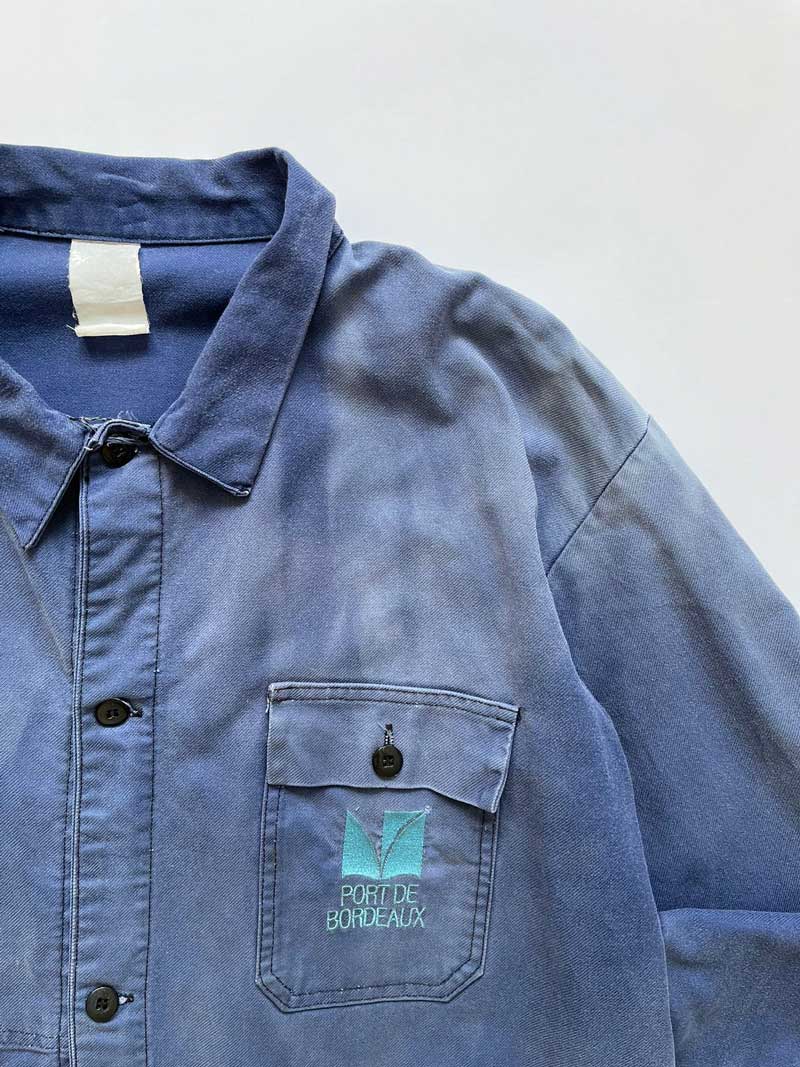 French work jacket from the 70s of Port De Bordeaux. Made from quality, durable cotton. The different shades of blue give a unique character to this jacket. Positioned on a neutral white background.