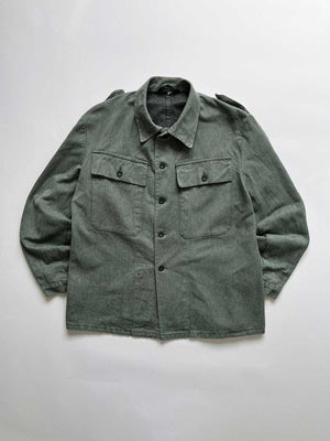 Swiss Army Denim Work Jacket produced from the 1950s to the 1990s by the Swiss Army. Color ranging from gray to greenish, made of thick, quality denim fabric. It has a workwear look but at the same time elegant, so it can be used in any situation. Positioned on a neutral white background.