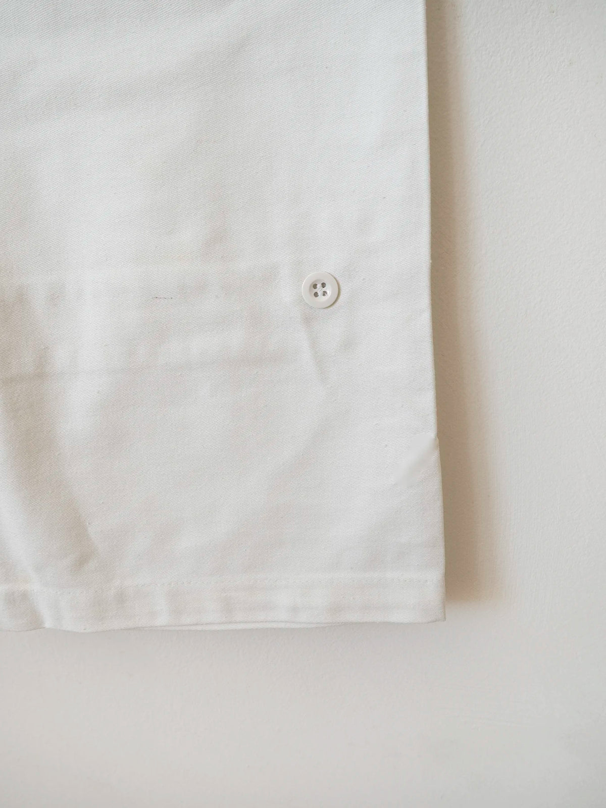 Dettaglio fondo gamba con bottone di chiusura dei pantaloni bianchi