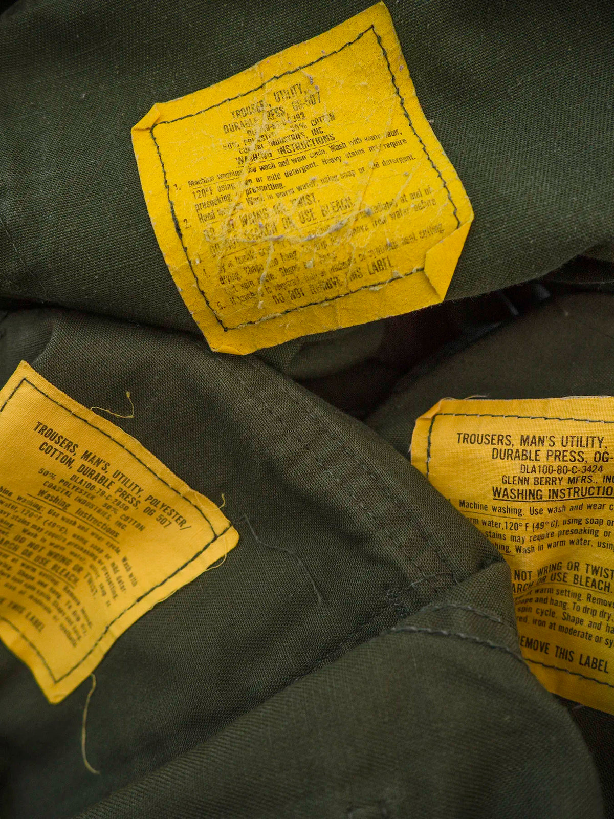 Confronto tra le etichette originali di più pantaloni OG 507, con numeri di contratto e produttori diversi
