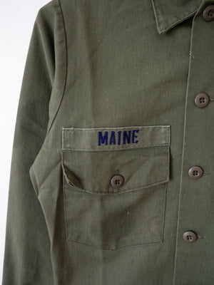 Detail of the woven 'Maine' name tape sewn above the left chest pocket of the vintage OG-507 shirt.