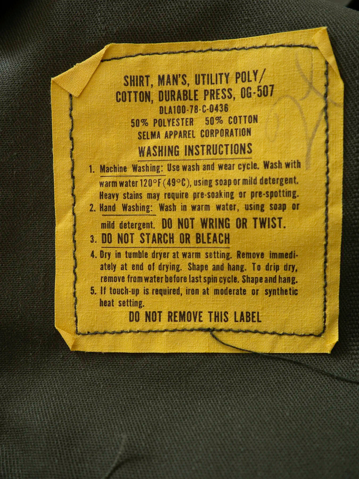 Original 1978 military label inside the OG-507 shirt, reading Shirt Man's Utility Poly Cotton Durable Press OG-507, Selma Apparel Corporation.