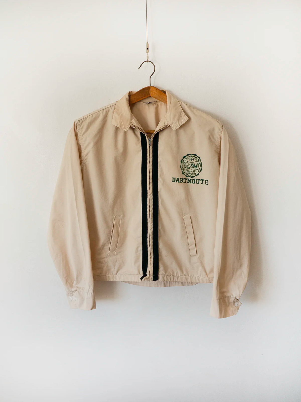 Vintage Dartmouth College Harrington jacket in light beige cotton, shown on a wooden hanger with the embroidered Dartmouth seal on the chest.