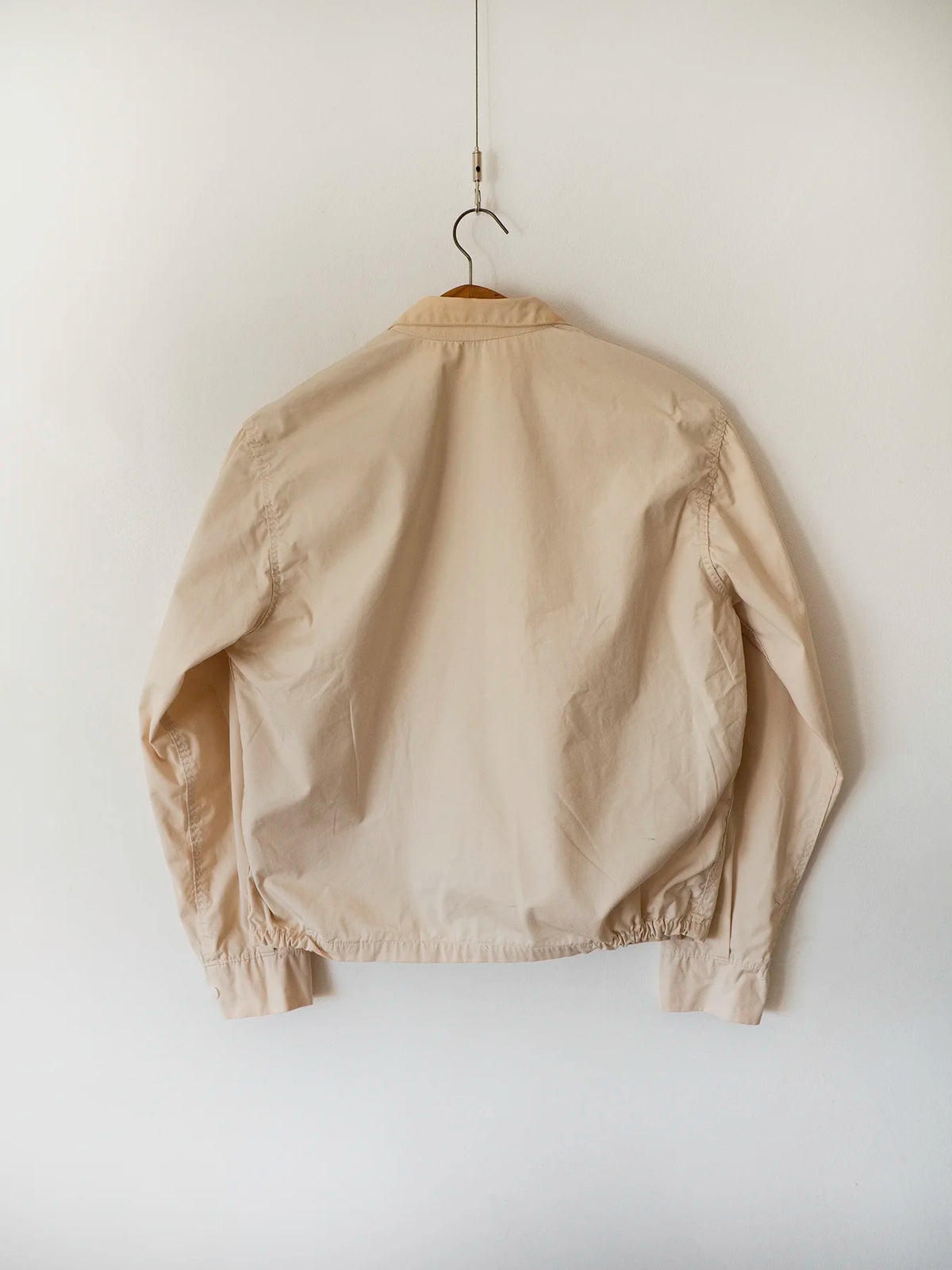 Back view of the vintage Dartmouth College Harrington jacket in light beige cotton, hung on a wooden hanger.